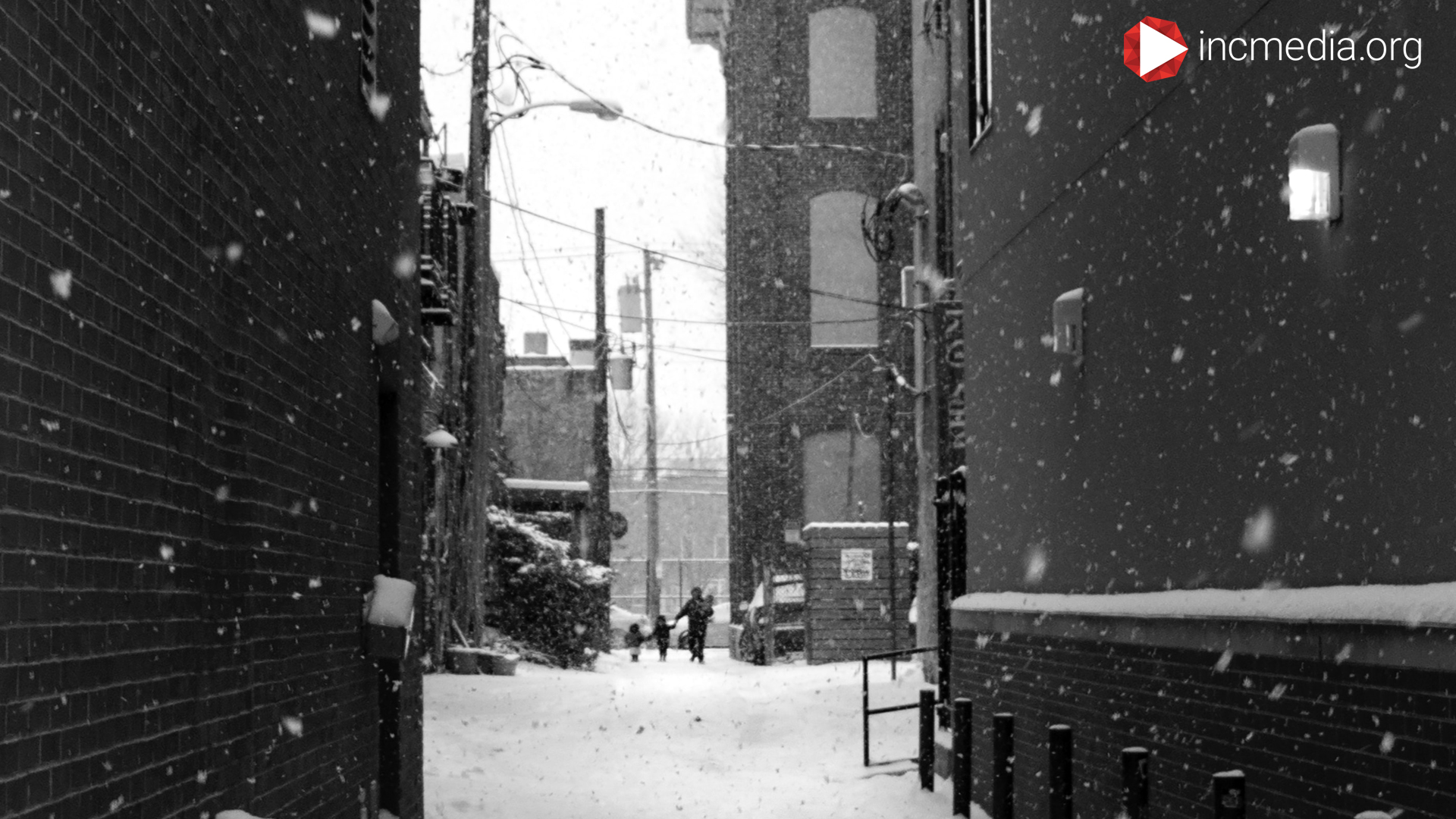 Alleyway with snow falling, a mom carrying three kids in the distance.