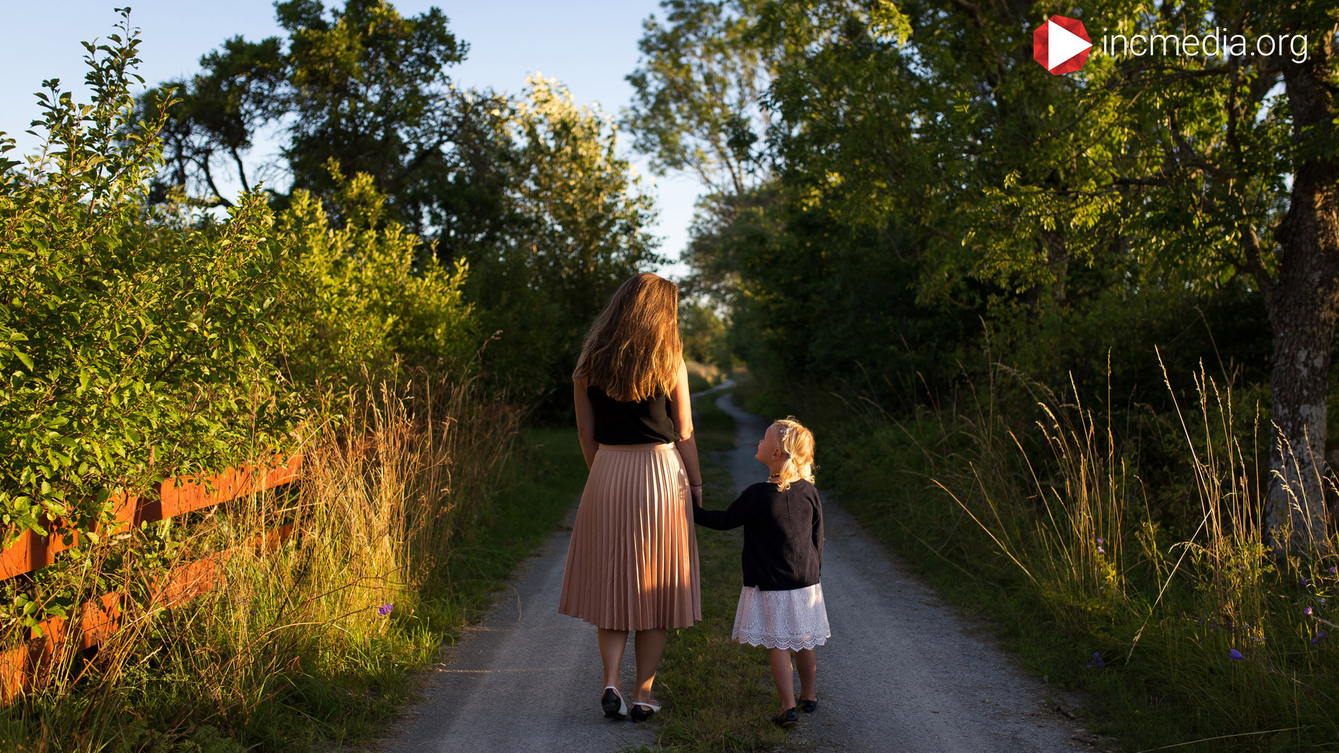 Mom and daughter walking down a path surrounded by trees