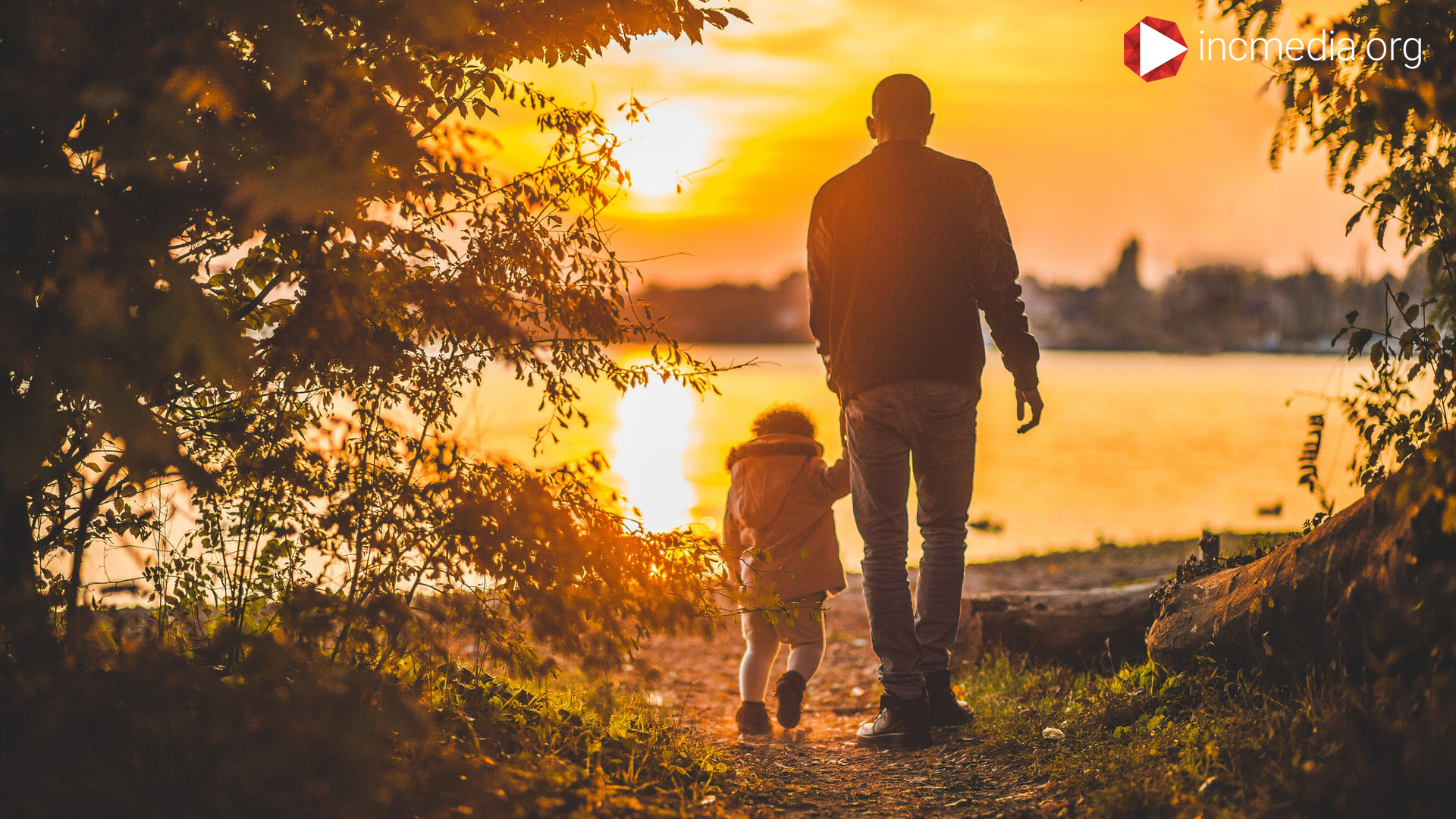 Man walking with a little kid into the sunset.