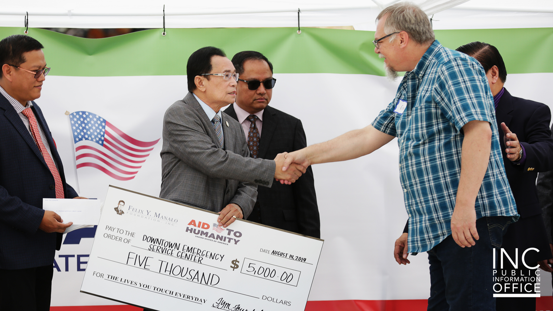 Two men shaking hands and exchanging a large donation check
