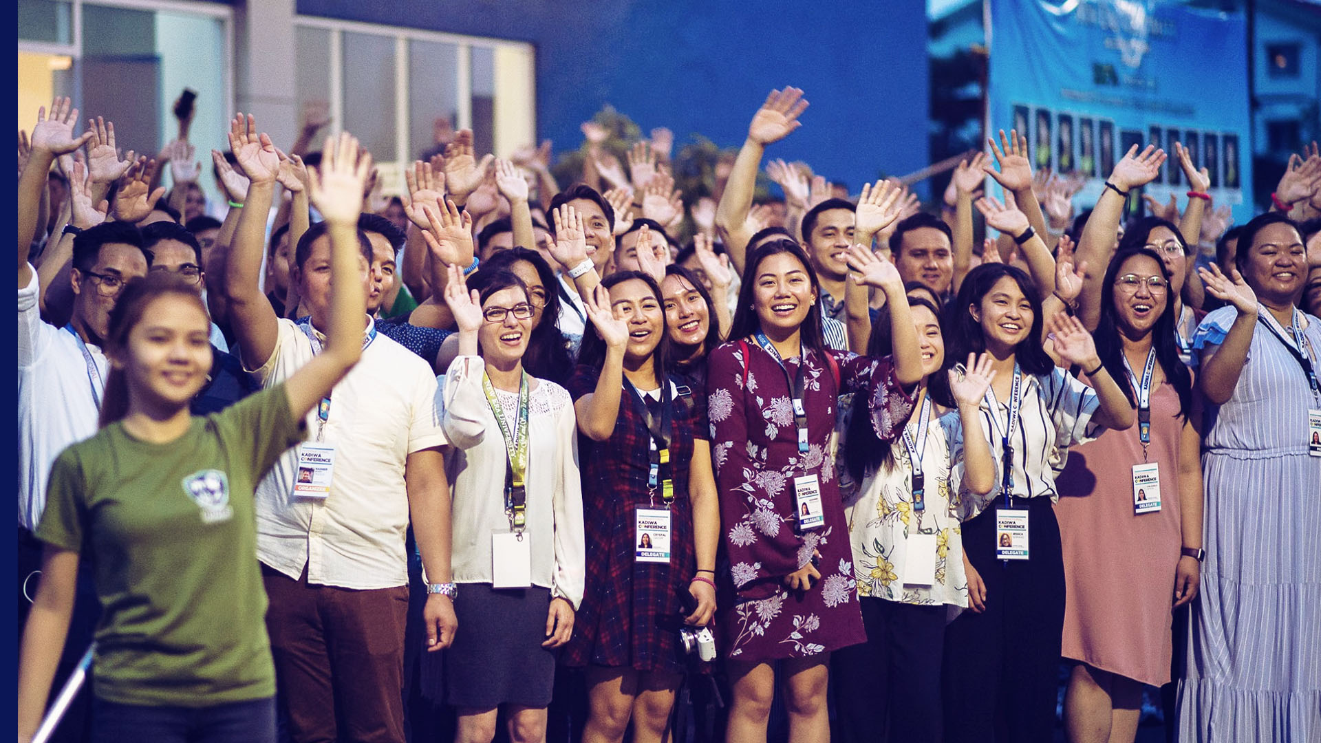 A group of young people in semi-formal attire waving to the camera and smiling